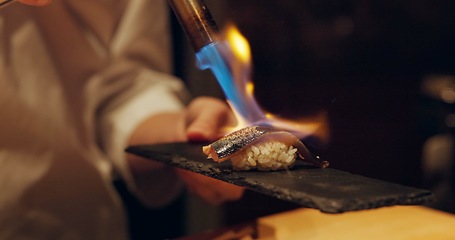 Image showing Hand, sushi and fire with chef in kitchen of restaurant for luxury or traditional cuisine closeup. Food, blow torch and cooking with person flame grilling fish or salmon for Japanese seafood meal