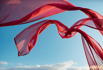 Image showing Flying transparent red fabric wave on blue sky background and il