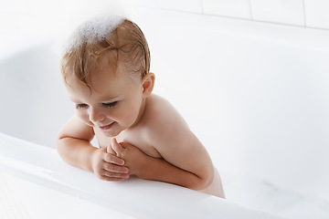 Image showing Happy baby in bathtub, cleaning and bubbles on mockup in morning routine for hygiene, wellness and body care in home. Cute toddler washing in foam with smile, relax and calm child in tub in bathroom.