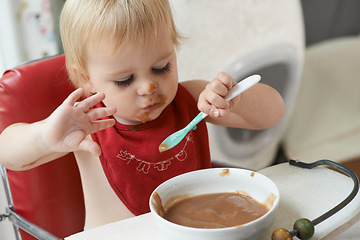 Image showing High chair, eating and baby with spoon in a house for nutrition, diet and fun while playing. Food, messy eater and boy kid at home with meal for child development, fiber or vitamins while learning
