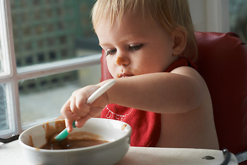 Image showing High chair meal, spoon and baby eating in a house with diet, nutrition and child development wellness. Food, messy eater and little boy kid curious about breakfast, playing or learning in his home
