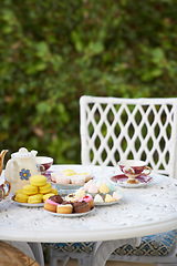 Image showing Table, tea party and cake in garden or cupcakes for birthday celebration, macarons or beverage. Backyard, chair and sweet dessert or food on patio or candy brunch for holiday relax, event or hungry