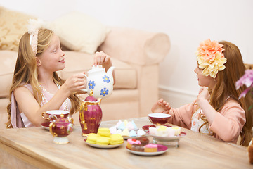 Image showing Girls, friends and playing tea party in home for fancy dress up fantasy for game, bonding or birthday. Female people, siblings and flower crown or pot for drinking or eat macarons, snack or chatting