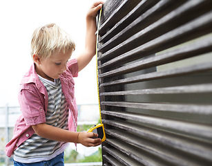 Image showing Cute, measuring tape and boy kid doing maintenance on wood gate for fun or learning. Focus, equipment and young child working on repairs with tool for home improvement outdoor at modern house.