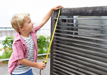 Image showing Cute, measuring tape and portrait child doing maintenance on wood gate for fun or learning. Happy, equipment and young boy kid working on repairs with tool for home improvement outdoor at house.