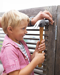 Image showing Happy, hammer and boy kid doing maintenance on wood gate for fun or learning. Smile, equipment and young child looking and working on repairs with tool for home improvement outdoor at modern house.