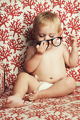 Image showing Glasses, playing and sweet baby in a studio with vision, health or eye care accessory for development. Cute, eyewear and young child, infant or toddler kid with spectacles by wallpaper background.