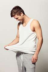 Image showing Smile, morning and pajamas with a young man in studio on a white background to wake up in a good mood. Relax, happy and casual with a person looking at his vest or tank top for weekend chilling