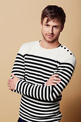 Image showing Fashion, crossed arms and portrait of man in studio in trendy, stylish and casual clothes on beige background. Confident, attractive and person in stripe style for positive attitude, pride and smile