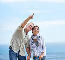 Image showing Pointing, happy couple and travel together at the beach with love, adventure and summer. Vacation, man and woman holding hands and sightseeing at ocean, offshore or enjoy holiday with support or care