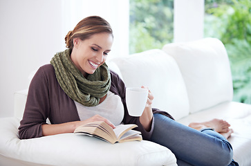 Image showing Happy, woman and reading book with coffee on sofa for story, novel or hobby in living room at home. Lady, fiction books and drinking cup of tea for literature, knowledge or comfortable break on couch