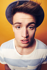 Image showing Portrait, hat and man with fashion, stylish clothes and confident guy on an orange studio background. Face, person and model with accessory, student and aesthetic with casual outfit, trendy and cool