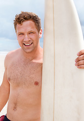 Image showing Portrait, happy and shirtless man with surfboard at beach on blue sky for sports, travel or fitness. Nature, smile and body of young person by ocean or sea for surfing, exercise and training