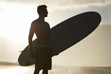 Image showing Surfing, sunset and silhouette of man at a beach with surfboard for freedom, travel or sports outdoor. Ocean, training and surfer shadow at sea for swimming, wellness or adventure, workout or holiday