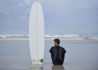 Image showing Beach, fitness and man thinking with a surfboard for wellness, sports and training while sitting in nature. Water, exercise and back of male surfer at the ocean with peace, calm and sea hobby in Bali