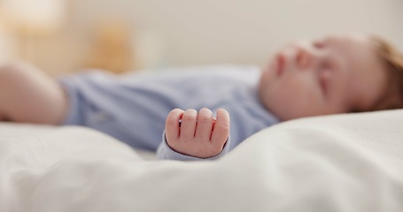 Image showing Hand, baby and sleeping on bed in nursery with relaxing, resting and nap on blanket in morning. Newborn, peaceful and dreaming in bedroom of home for child development, growth and nurture or relax