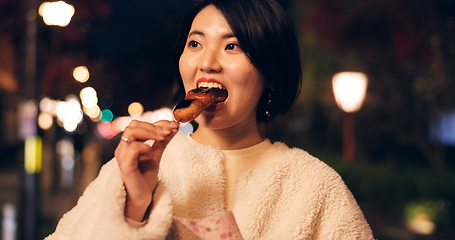 Image showing Woman, street food and eating Japanese snack for travel experience, hungry or local trip. Female person, sidewalk and night or bite grilled mochi on road for vacation culture, adventure or tradition