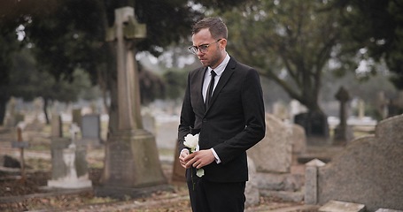 Image showing Funeral, cemetery and man with flower by tombstone for remembrance, burial ceremony and memorial service. Depression, sad and person with rose by gravestone for mourning, grief and loss in graveyard