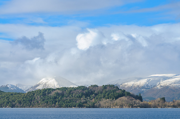 Image showing Snow-capped mountains towering behind a dense forest by the calm