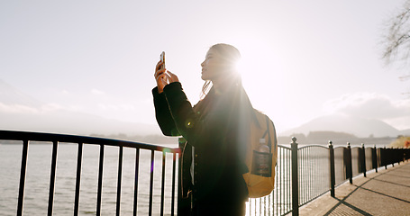 Image showing Japanese woman, lake and phone for photography, memory and post on web blog for travel with backpack. Girl, person and outdoor with smartphone by water, river and photoshoot for social media in Tokyo