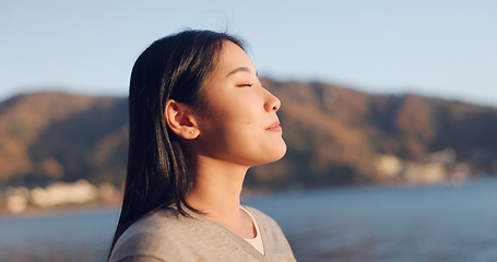 Image showing Japanese woman, breathing and peace outdoor, lake or ocean with travel, holiday and mindfulness in nature. Wellness, adventure and care free at beach in Japan, calm with freedom and positivity