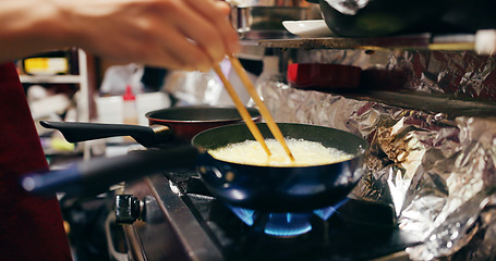 Image showing Cooking, chopsticks and person with pan on gas stove at market for meal preparation, eating and nutrition. Culinary, flame and closeup of chef hands with utensils for egg cuisine, dinner and supper