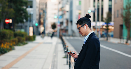 Image showing Phone, networking and Japanese businessman in the city reading company email on technology. Career, travel and professional young male person scroll or browse on cellphone with earbuds in urban town.