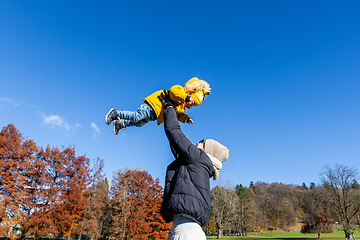 Image showing More, more,...mum, that's fun. Happy young mother throws her cute little baby boy up in the air. Mother's Day, Mather and her son baby boy playing and hugging outdoors in nature in fall.