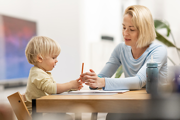 Image showing Caring young Caucasian mother and small son drawing painting in notebook at home together. Loving mom or nanny having fun learning and playing with her little 1,5 year old infant baby boy child.