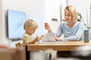 Image showing Caring young Caucasian mother and small son drawing painting in notebook at home together. Loving mom or nanny having fun learning and playing with her little 1,5 year old infant baby boy child.