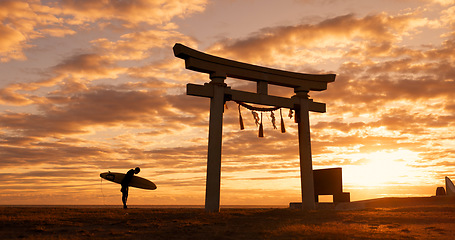 Image showing Torii gate, sunset and man with surfboard bowing, ocean and travel adventure in Japan with orange sky. Shinto architecture, Asian culture and calm beach in Japanese nature with person at spiritual mo