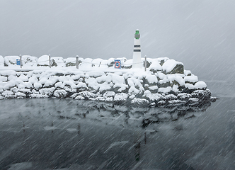 Image showing A lighthouse stands resilient as snow covers the surrounding landscape amidst a winter storm.