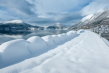 Image showing A serene snowy landscape showcases a pathway bordered by undisturbed snow drifts with mountains reflected in the calm sea.