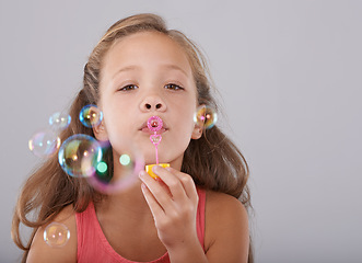Image showing Portrait, little child and blowing bubbles in studio by toy, cute and fun games with soap liquid. Girl, face and learning to play with bubble wand, childhood development and sweet by gray background