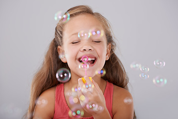 Image showing Happy, little girl and blowing bubbles in studio by toy, cute and fun games for hand eye coordination. Child, eyes closed and play with bubble wand, childhood development and smile by gray background