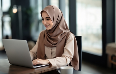 Image showing In a cozy cafe, a woman in a hijab embraces modernity as she diligently works on her laptop, seamlessly blending technology with tradition in a contemporary and culturally diverse workspace