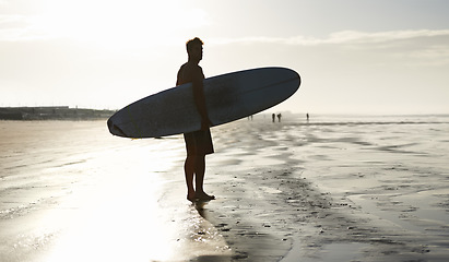 Image showing Sunset, surfing and silhouette of man at a beach with surfboard for freedom, travel or sports outdoor. Ocean, training and surfer shadow at sea for swimming, wellness or adventure, workout or holiday