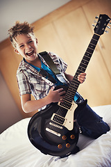 Image showing Happy, portrait and child with guitar on bed for music lesson or practice at modern home. Fun, rockstar and young boy kid playing electric string instrument for concert in bedroom for hobby at house.