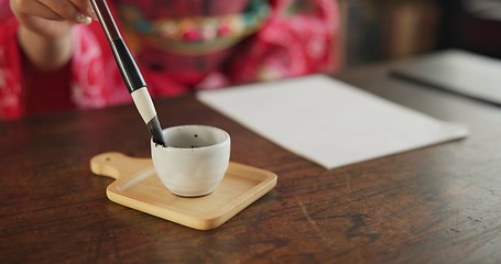 Image showing Ink, writing and hands of Japanese woman in home for traditional script on paper, documents and page. Creative, culture and person with vintage paintbrush tools for calligraphy, font or text in house