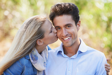 Image showing Happy couple, portrait and kiss on cheek in nature for love, bonding or support in relax for outdoor affection. Face of young woman and man smile for embrace, intimacy or romance in forest together