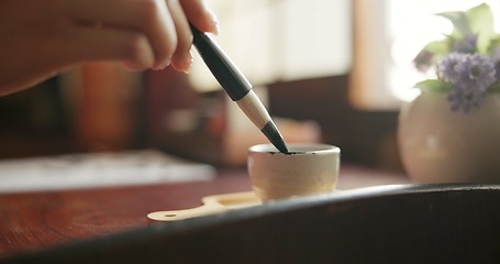 Image showing Brush, closeup and hands at a table for calligraphy, writing or ancient Japanese art in a house. Letter, communication and zoom on person fingers with traditional ink stroke, penmanship or art tool