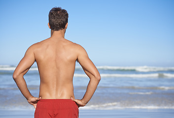 Image showing Man, lifeguard and beach for security, emergency or outdoor swimming in health and safety. Rear view or back of male person or professional swimmer stranding ready for patrol at sea or ocean coast