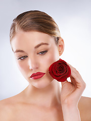 Image showing Face, rose and red lipstick makeup with woman in studio on gray background for cosmetology. Beauty, aesthetic and flower with confident young model at salon or spa for natural cosmetic makeover