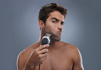 Image showing Man, shaving and machine in studio for beard grooming, skincare and portrait by grey background. Person, model and self care for hygiene, facial hair removal and electric razor for cosmetic change