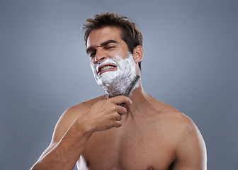 Image showing Man, shaving and pain in studio portrait with grooming, skincare and wellness with stress by grey background. Person, model and anxiety with beard, facial hair removal and product for cosmetic change