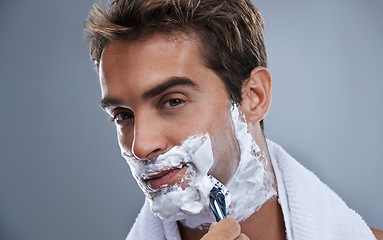 Image showing Man, blade and shaving beard in studio closeup for grooming, skincare and portrait by grey background. Person, model and self care with cream, facial hair removal and product for cosmetic change