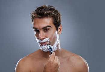 Image showing Man, razor and face with shaving in studio portrait for grooming, skin and wellness by grey background. Person, model and blade with cream, facial hair removal and foam product for hygiene with beard