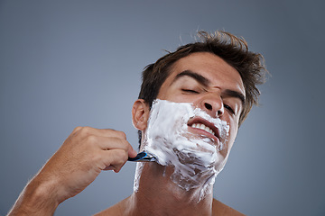 Image showing Man, shaving and stress with razor in studio portrait for wellness, skin and grooming by grey background. Person, model and frustrated with beard, facial hair removal and product for cosmetic change