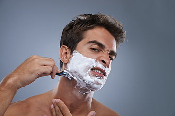 Image showing Man, shaving and frustrated with razor in studio portrait for wellness, skin and grooming by grey background. Person, model and stress with beard, facial hair removal and product for cosmetic change