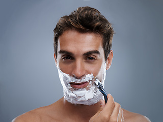 Image showing Man, razor and shaving beard in studio portrait for grooming, skincare and wellness by grey background. Person, model and blade with cream, facial hair removal and foam product for cosmetic change